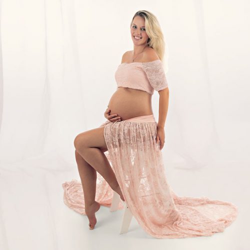 schwangere Frau im rosa Kleid, das auf einem Stuck sitzt